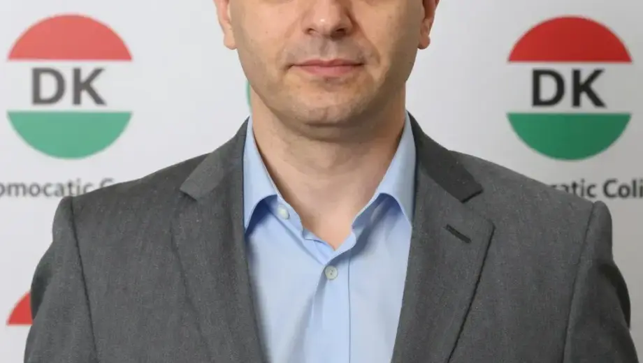 A portrait of Nyakó István, a Hungarian politician, standing confidently in front of a backdrop featuring the DK (Democratic Coalition) party logo and Hungarian political symbols, with a clear, professional appearance and a serious yet approachable expression, captured in high detail