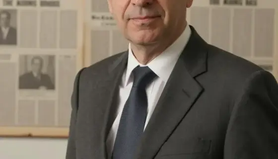 A solemn portrait of a middle-aged male journalist with short dark hair and glasses, wearing a formal suit, standing in front of a vintage newspaper office background with old papers and a typewriter, conveying a sense of respectful remembrance
