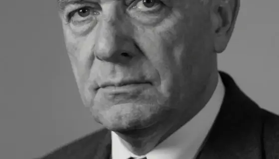 A somber black and white portrait of a 68-year-old man, László Varga, with a serious expression, looking slightly to the side, wearing formal attire from the mid-20th century, soft lighting, high detail, emotional atmosphere, subtle grain texture
