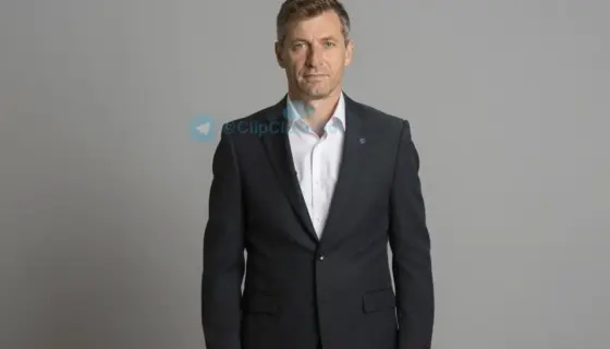 A formal portrait of a Hungarian sports patron (mecénás) from 2017, dressed in a classic suit with a subtle sports emblem on the lapel, standing in a dignified pose against a neutral background, conveying support for sports development
