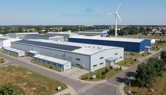A detailed view of the Miskolc South Industrial Park infrastructure, showing modern industrial buildings, clean energy installations like solar panels or wind turbines, well-maintained roads and pathways, green spaces with trees and grass, and signage indicating the park's name, all under a clear daytime sky