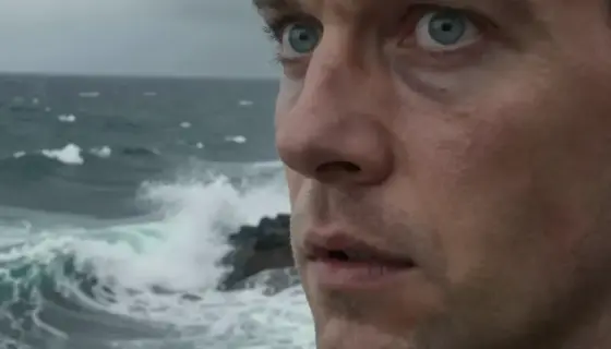 A dramatic close-up of a man with intense, wide eyes reflecting the sea, standing on a rocky cliff overlooking a turbulent ocean during a storm, with dark clouds and crashing waves, emphasizing the moment of shock or awe as if his eyes were 'blinded by the sea', in a realistic and detailed style