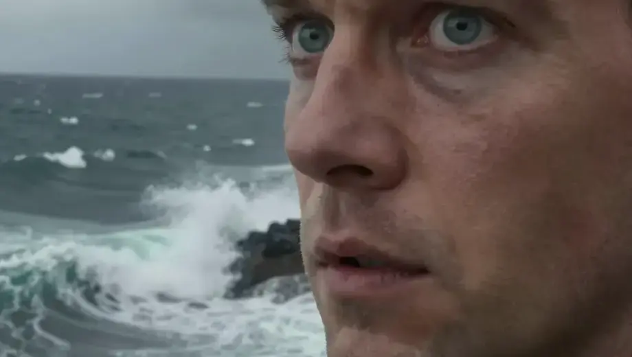 A dramatic close-up of a man with intense, wide eyes reflecting the sea, standing on a rocky cliff overlooking a turbulent ocean during a storm, with dark clouds and crashing waves, emphasizing the moment of shock or awe as if his eyes were 'blinded by the sea', in a realistic and detailed style