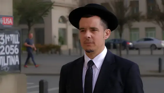 A solemn Jewish man in traditional attire (kippah, suit) standing in a modern German city square, with subtle antisemitic graffiti on a nearby wall, muted colors, serious expression, photorealistic detail