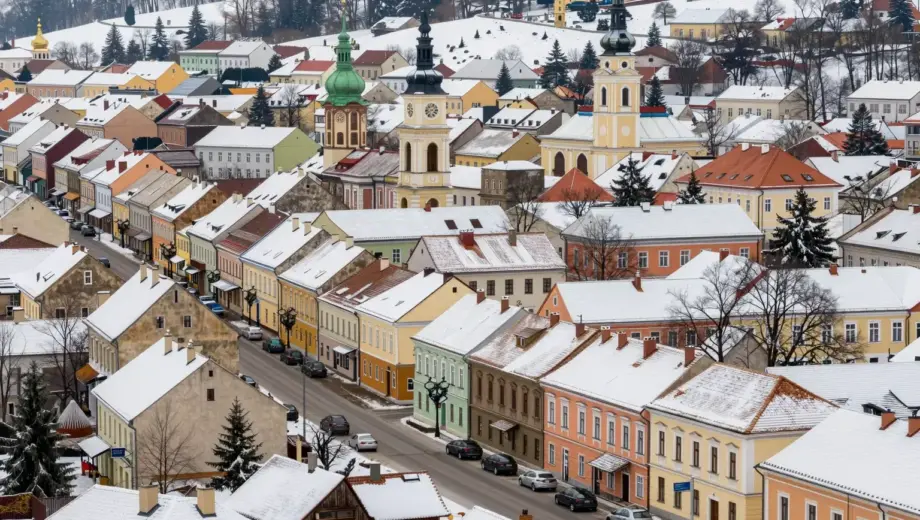 A vibrant and detailed scene showcasing the city of Miskolc and its surrounding area during the winter season. The image should capture the essence of the region, including its architecture, natural landscapes, and cultural elements. Snow-covered streets, traditional buildings, and local landmarks should be prominently featured. The atmosphere should be warm and inviting, highlighting the beauty of Miskolc in winter.