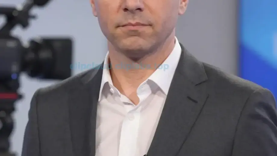 A portrait of Petroczi Attila, a Hungarian television presenter, shown in a 37-second video clip still. He is wearing formal attire, likely a suit, with a serious or professional expression. The image should capture his upper body and face clearly, with studio lighting and a neutral background. The scene should reflect a broadcast or television studio setting, with possible visible elements like a camera, microphone, or monitor in the background. The image must be clear and high-resolution, emph