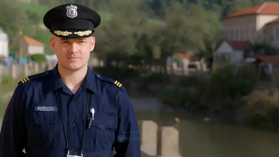 A realistic portrait of a Hungarian police officer in a traditional uniform standing in Borsod-Abaúj-Zemplén County, with a subtle transformation effect showing personal changes in their career, set in a natural outdoor environment with local landmarks like the Borsod River or historic buildings, emphasizing professional dedication and community connection
