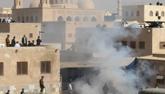 A historical scene depicting liquidation operations in a Middle Eastern city, showing armed soldiers or officials conducting raids on buildings, with smoke rising from structures, people being detained or displaced, and military vehicles present, set against a backdrop of traditional architecture with minarets and domes, conveying tension and urgency