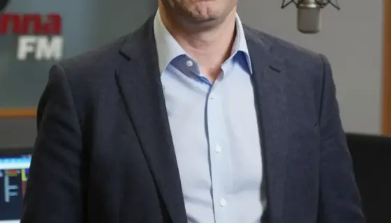 A portrait of Viktor Hamvas, the program director of Manna FM radio station, shown in a professional studio setting with broadcasting equipment like microphones and mixing consoles in the background, wearing formal attire with a serious but approachable expression, natural lighting highlighting his face, medium shot composition