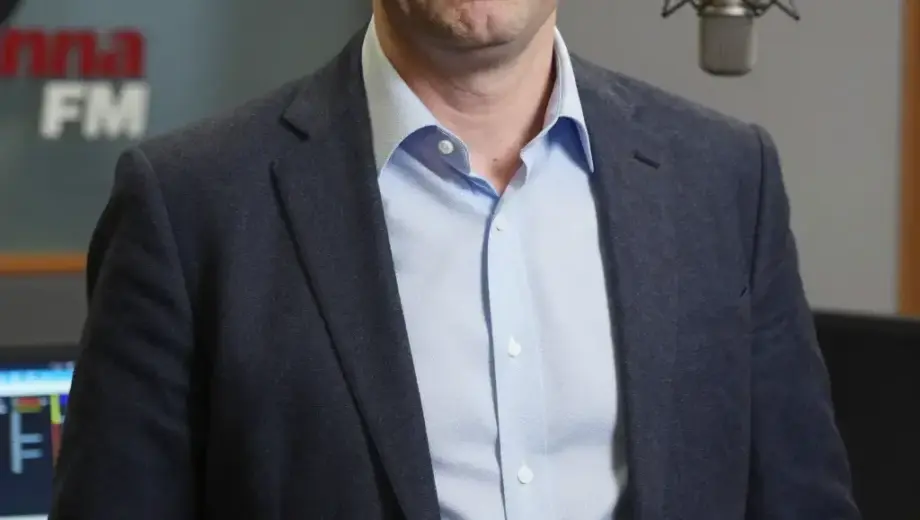 A portrait of Viktor Hamvas, the program director of Manna FM radio station, shown in a professional studio setting with broadcasting equipment like microphones and mixing consoles in the background, wearing formal attire with a serious but approachable expression, natural lighting highlighting his face, medium shot composition