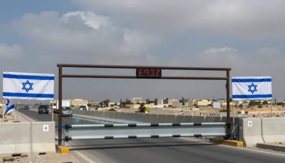 A symbolic image showing a closed border crossing with Israeli flags and barriers, representing the refusal to open the Erez crossing, with a tense atmosphere and distant Gaza Strip in the background under a cloudy sky