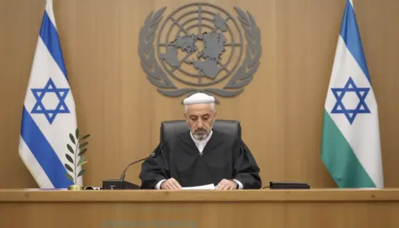 A solemn international courtroom scene with the United Nations emblem visible in the background, a judge in traditional robes presiding, and symbolic representations of Israel and Hamas — such as a broken olive branch and a torn flag — placed on either side of the bench, conveying impartial judgment under international law, soft natural lighting, dignified atmosphere, no text or symbols on clothing or flags