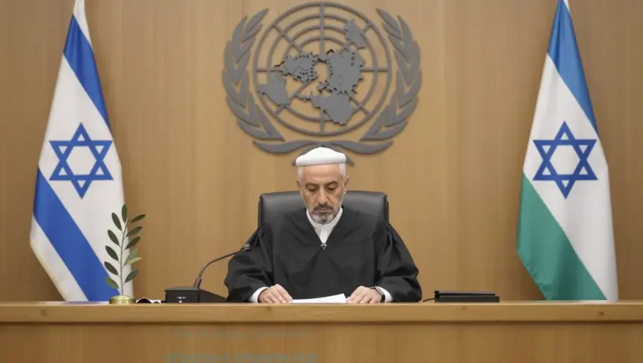 A solemn international courtroom scene with the United Nations emblem visible in the background, a judge in traditional robes presiding, and symbolic representations of Israel and Hamas — such as a broken olive branch and a torn flag — placed on either side of the bench, conveying impartial judgment under international law, soft natural lighting, dignified atmosphere, no text or symbols on clothing or flags