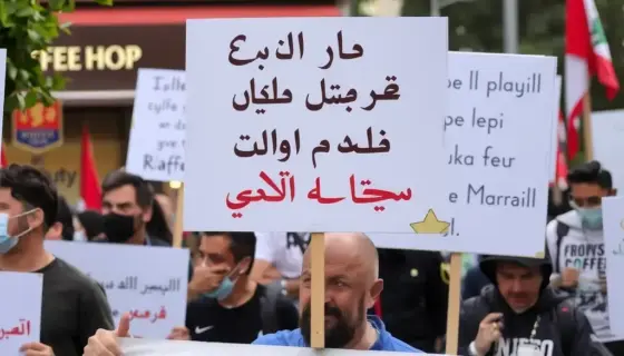 A street protest in Lebanon with people holding signs, a coffee shop visible in the background