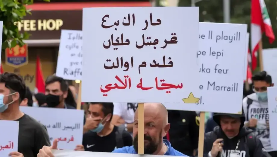 A street protest in Lebanon with people holding signs, a coffee shop visible in the background